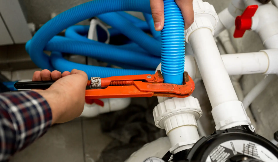 Closeup shot of plumber connecting two pipes with red pliers