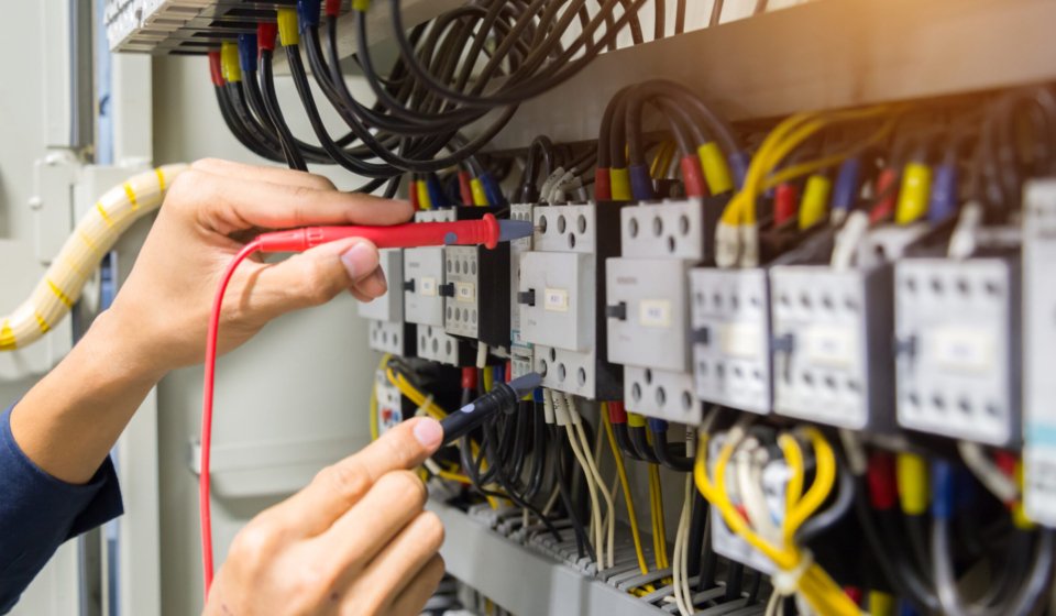Electricians hands testing current electric in control panel.
